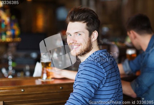 Image of happy young man drinking beer at bar or pub