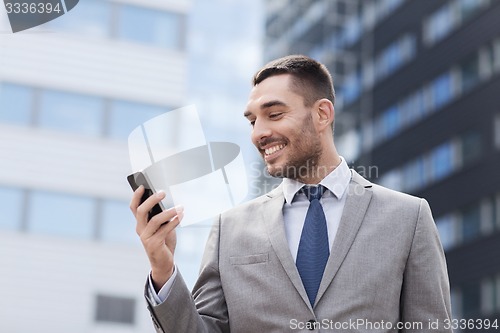 Image of smiling businessman with smartphone outdoors