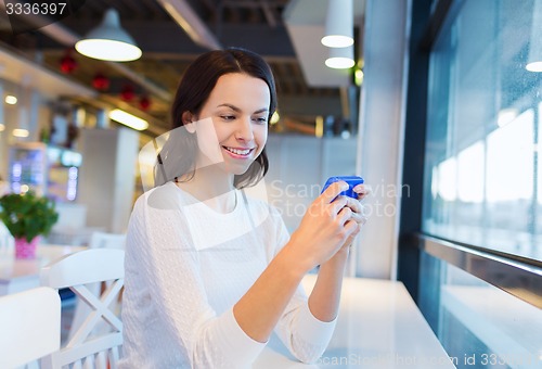 Image of smiling woman with smartphone at cafe