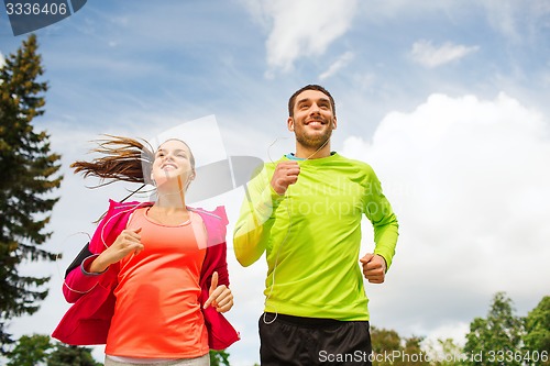 Image of smiling couple with earphones running outdoors