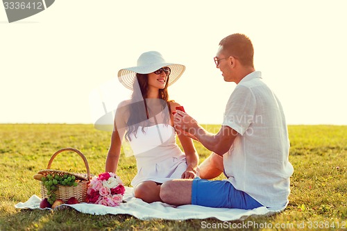 Image of smiling couple with small red gift box on picnic