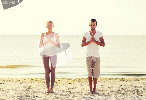 Image of smiling couple making yoga exercises outdoors