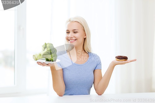 Image of smiling woman with broccoli and donut at home