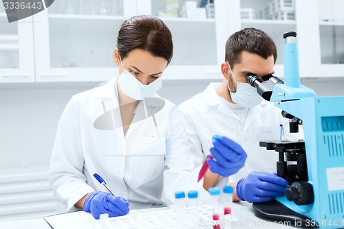 Image of scientists with clipboard and microscope in lab