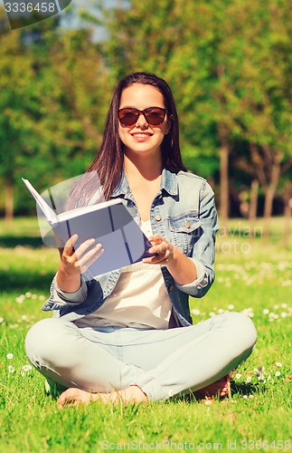 Image of smiling young girl with book sitting in park