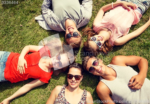 Image of group of smiling friends lying on grass outdoors