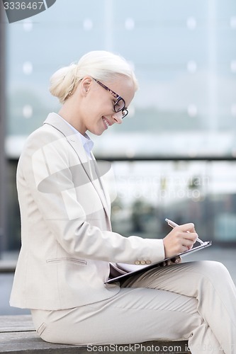 Image of young smiling businesswoman with notepad outdoors