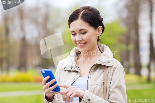 Image of smiling woman calling on smartphone in park