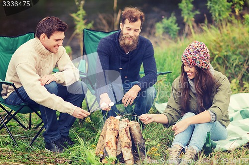 Image of smiling tourists cooking marshmallow in camping