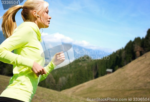 Image of happy young woman with earphones jogging outdoors