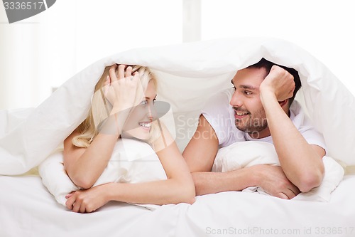 Image of happy couple lying in bed and talking at home