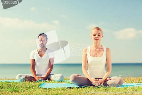 Image of smiling couple making yoga exercises outdoors