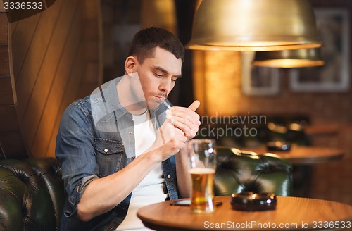 Image of man drinking beer and smoking cigarette at bar