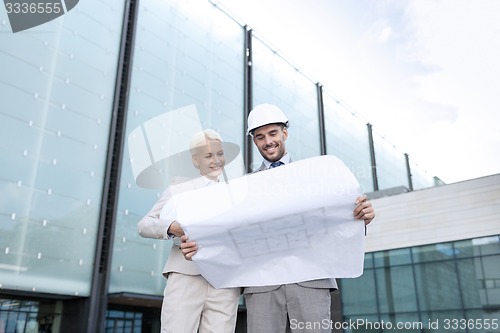 Image of smiling businessmen with blueprint and helmets