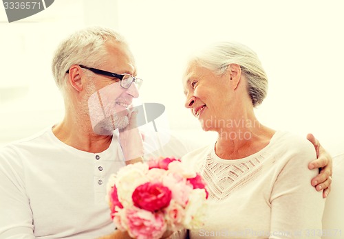 Image of happy senior couple with bunch of flowers at home