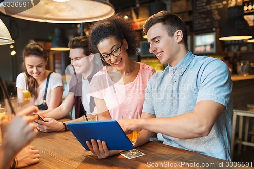 Image of happy friends with tablet pc and drinks at bar