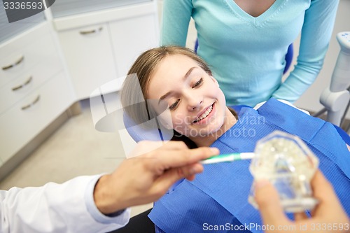 Image of happy dentist showing toothbrush to patient girl