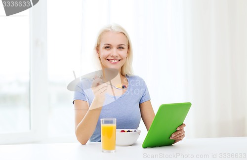 Image of smiling woman with tablet pc eating breakfast