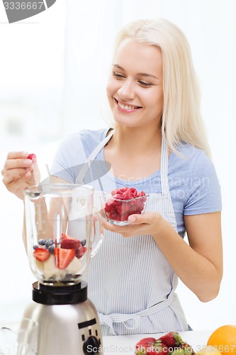 Image of smiling woman with blender preparing shake at home