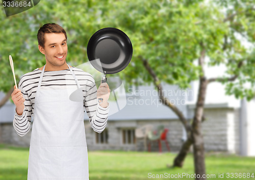 Image of happy man or cook in apron with pan and spoon