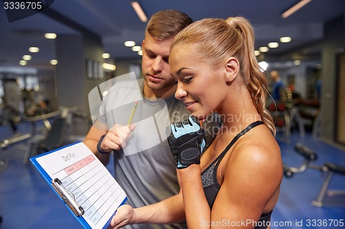 Image of smiling woman with trainer and clipboard in gym