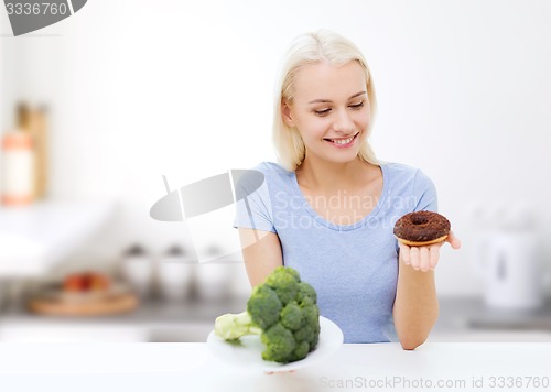 Image of smiling woman with broccoli and donut on kitchen