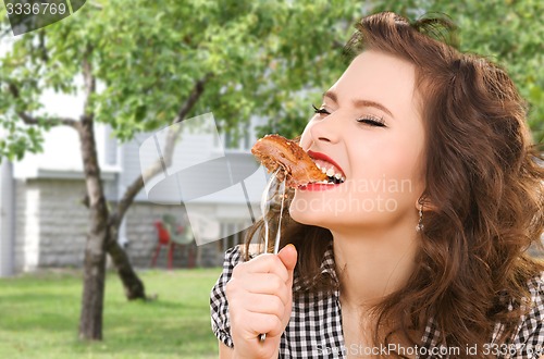 Image of hungry young woman eating meat on fork over house
