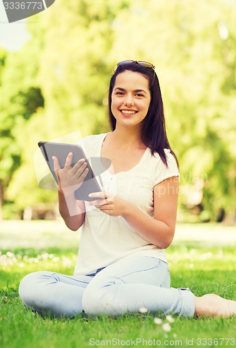 Image of smiling young girl with tablet pc sitting on grass