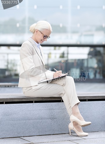 Image of young smiling businesswoman with notepad outdoors