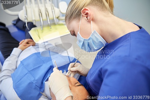 Image of female dentist in mask checking male patient teeth