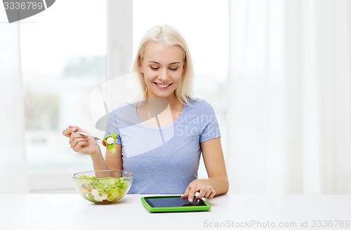 Image of smiling woman eating salad with tablet pc at home