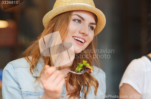 Image of happy young woman eating salad at bar or pub