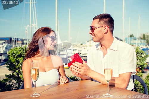 Image of smiling couple with champagne and gift at cafe