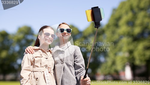 Image of happy girls with smartphone selfie stick in park