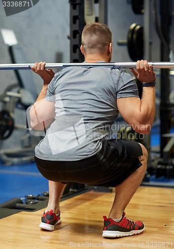 Image of young man flexing muscles with barbell in gym