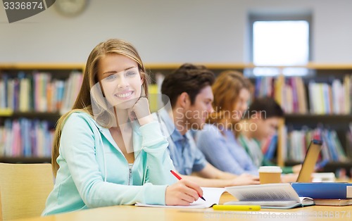 Image of happy student girl writing to notebook in library