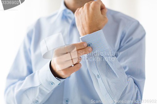 Image of close up of man fastening buttons on shirt sleeve