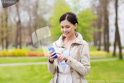 Image of smiling woman calling on smartphone in park