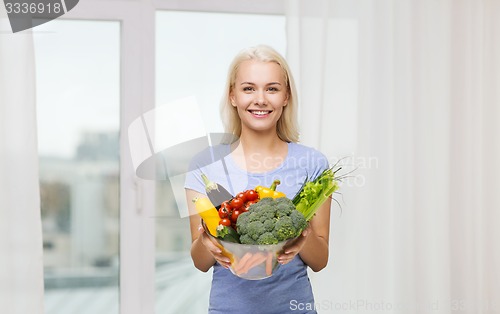 Image of smiling young woman with vegetables at home