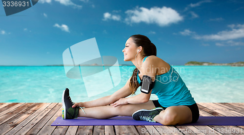 Image of smiling woman stretching leg on mat over sea