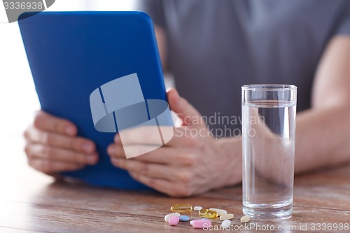 Image of close up of hands with tablet pc, pills and water