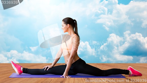 Image of smiling woman doing splits on mat over clouds