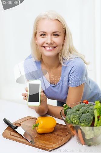 Image of smiling woman with smartphone cooking vegetables