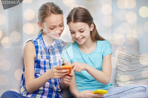 Image of happy girls with smartphones sitting on sofa