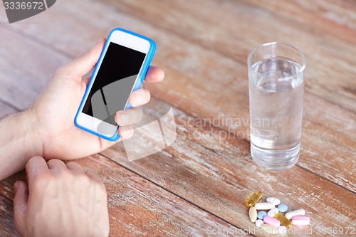 Image of close up of hands with smartphone, pills and water