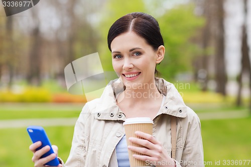 Image of smiling woman with smartphone and coffee in park