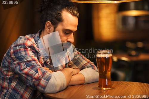 Image of unhappy lonely man drinking beer at bar or pub