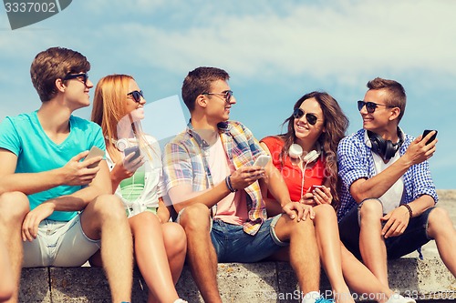 Image of group of smiling friends with smartphones outdoors