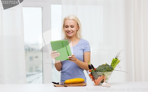 Image of smiling young woman with tablet pc cooking at home