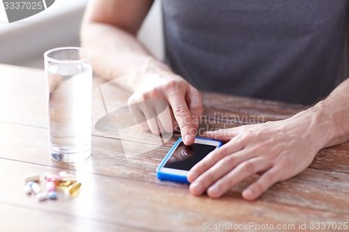 Image of close up of hands with smartphone, pills and water